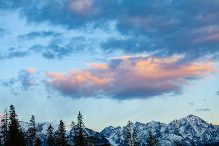 A fabulous cloud hanging over the snowy peaks, illuminated by the setting sun. Beautifully harmonious colors.の写真素材