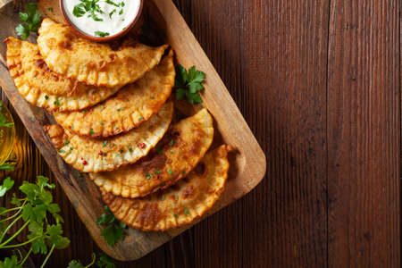 Traditional cheebureki, served on a wooden plate with sauce. Decorated with parsley.