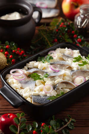 Herring fillet salad in cream with apple. Served in a black briquette. Wooden background. Christmas decoration.の写真素材