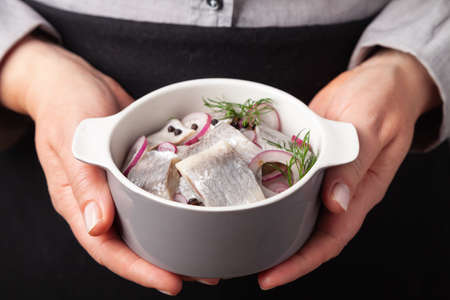 The cook serves herring fillets in oil with onions in a bowl. She holds the food in her hands.の写真素材