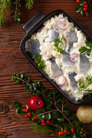 Herring fillet salad in cream with apple. Served in a black briquette. Wooden background. Christmas decoration.の写真素材