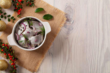 Herring fillets in oil. Served with onion in a bowl. Wooden background. Christmas decorationの写真素材