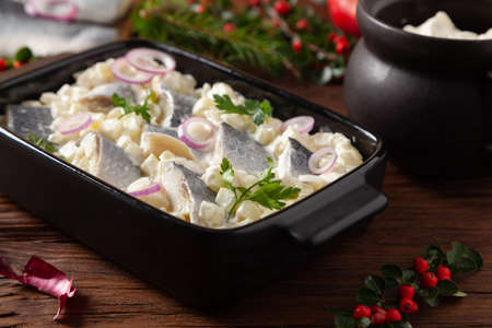 Herring fillet salad in cream with apple. Served in a black briquette. Wooden background. Christmas decoration.の写真素材