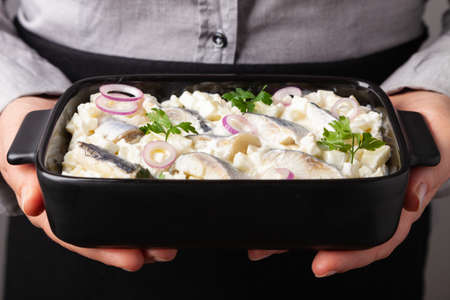 The cook serves fillet salad in cream with apple in a bowl. She holds the food in her hands.の写真素材