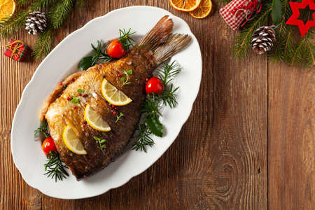 Fried carp whole. Served with lemon and cherry tomatoes on white plate. Christmas decoration. Top...