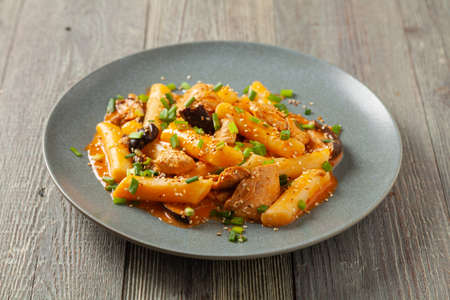 Traditional Korean Tteokbokki rice noodles with chicken, vegetables and shitake mushrooms. Prepared in a pan. Wooden background. Front view.の写真素材