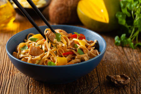 Fried chicken with mango and coconut milk with noodles. Prepared in a wok. Front view. Served in a blue bowl.の写真素材