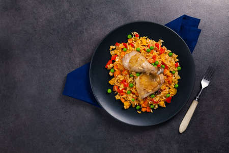 Arroz con pollo. Baked pieces of chicken with bone, rice with paprika and peas. Black background. Served on black plate or spanish pan.の写真素材