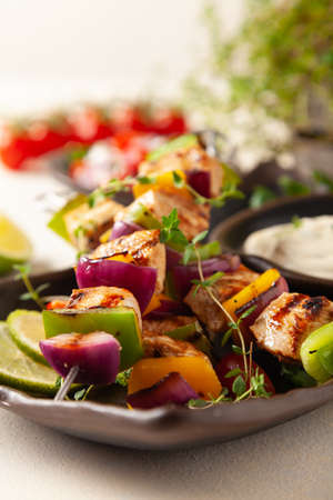 Grilled skewers with chicken, pepper, and onion. Served with sauce. Painted, bright background.の写真素材