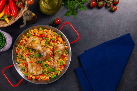 Arroz con pollo. Baked pieces of chicken with bone, rice with paprika and peas. Black background. Served on black plate or spanish pan.の写真素材