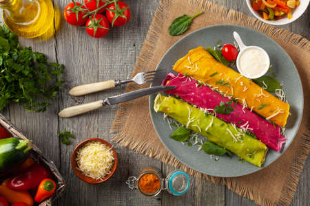 Colorful pancakes with chicken and lb vegan stuffing. Naturally colored with juice or seasoning. Served with sauce or yoghurt. Wooden background.の写真素材