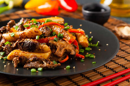 Traditional Korean Tteokbokki rice noodles with beef, vegetables and shitake mushrooms. Prepared in a wok. Dark blue background.の写真素材