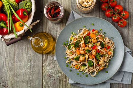 stir-fry pasta with chicken, broccoli and carrots. Top view. Gray wooden background. Served on a gray plate.の写真素材
