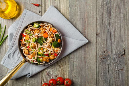 stir-fry pasta with chicken, broccoli and carrots. Top view. Gray wooden background. Served in a frying pan.の写真素材