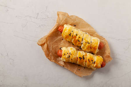 Sausage baked in puff pastry. Sprinkled with sesame seeds, served with sauce. Stone background.の写真素材