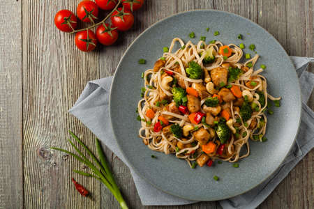 stir-fry pasta with chicken, broccoli and carrots. Top view. Gray wooden background. Served on a gray plate.の写真素材