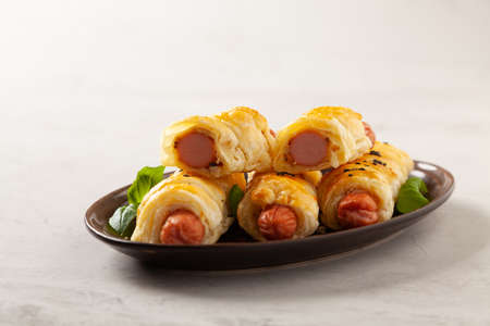 Sausage baked in puff pastry. Sprinkled with sesame seeds, served with sauce. Stone background.の写真素材