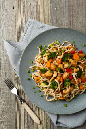 stir-fry pasta with chicken, broccoli and carrots. Top view. Gray wooden background. Served on a gray plate.の写真素材
