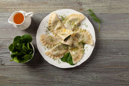 Dumplings with spinach, topped with melted butter and sprinkled with chopped dill. Wooden background. White plate.の写真素材