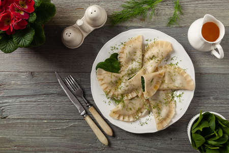 Dumplings with spinach, topped with melted butter and sprinkled with chopped dill. Wooden background. White plate.の写真素材