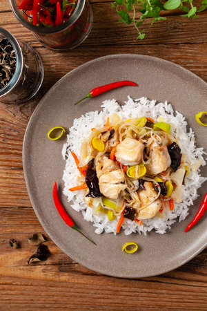 Chinese style cod, served on a plate with white rice. Natural wooden background.の写真素材