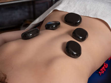 The masseuse gives a back massage with hot stones to a woman in a massage parlor. The patient is...