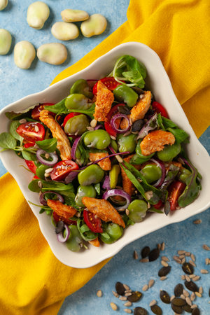 Delicious salad with broad beans and chicken. Served in a bowl on a blue painted background.の写真素材