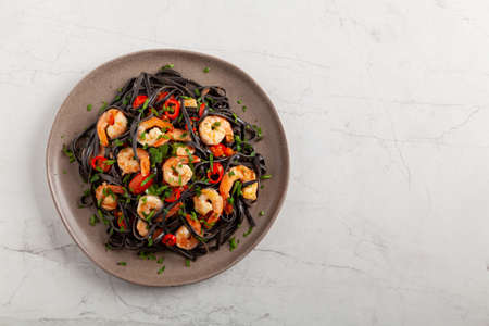 Black pasta with roasted prawns. Served on a plate. Stone background. Chopsticks or fork.の写真素材