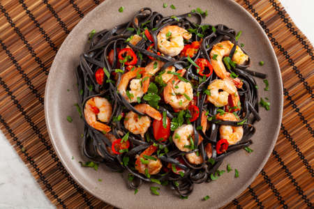 Black pasta with roasted prawns. Served on a plate. Stone background. Chopsticks or fork.の写真素材