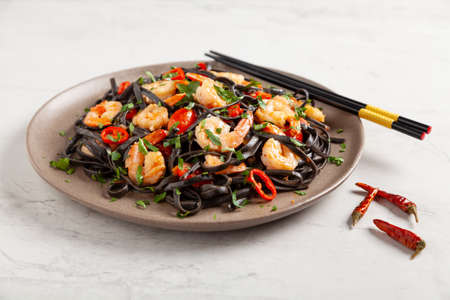 Black pasta with roasted prawns. Served on a plate. Stone background. Chopsticks or fork.の写真素材