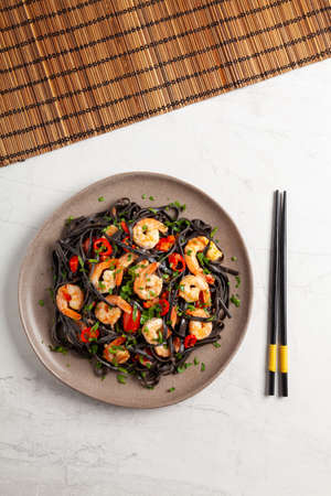 Black pasta with roasted prawns. Served on a plate. Stone background. Chopsticks or fork.の写真素材