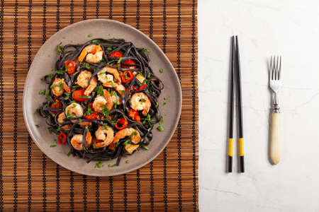 Black pasta with roasted prawns. Served on a plate. Stone background. Chopsticks or fork.の写真素材