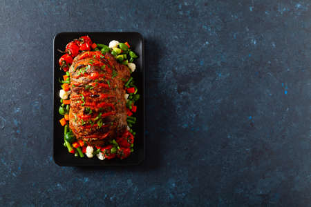 Whole roasted, stuffed with tomatoes and olives, pork neck. Dark background, dark mood.の写真素材