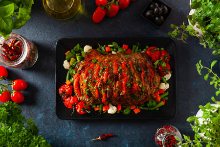 Whole roasted, stuffed with tomatoes and olives, pork neck. Dark background, dark mood.の写真素材