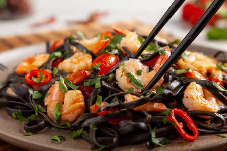 Black pasta with roasted prawns. Served on a plate. Stone background. Chopsticks or fork.の写真素材