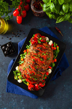 Whole roasted, stuffed with tomatoes and olives, pork neck. Dark background, dark mood.の写真素材