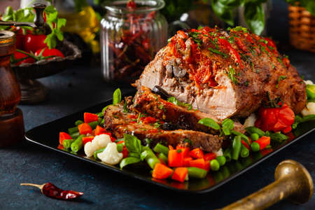Whole roasted, stuffed with tomatoes and olives, pork neck. Dark background, dark mood.の写真素材