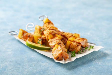 Grilled shashlik with salmon and pineapple. Served on paper try. Blue painted background.の写真素材