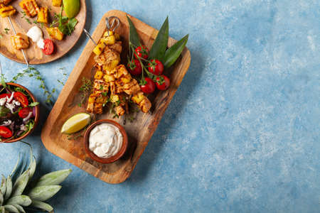 Grilled shashlik with salmon and pineapple. Served with yoghurt sauce. Blue painted background.の写真素材