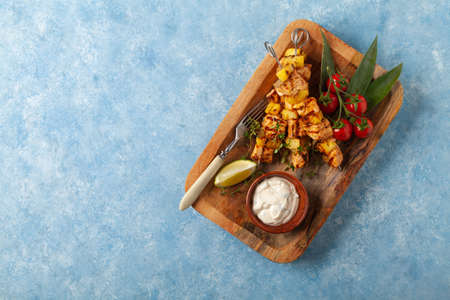 Grilled shashlik with salmon and pineapple. Served with yoghurt sauce. Blue painted background.の写真素材