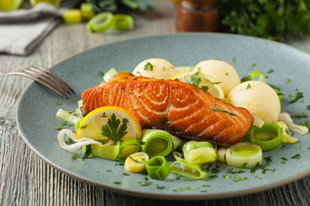 Portion of fried salmon, served with mashed potatoes and cooked leek. Front view. Gray plate, wooden background.の写真素材