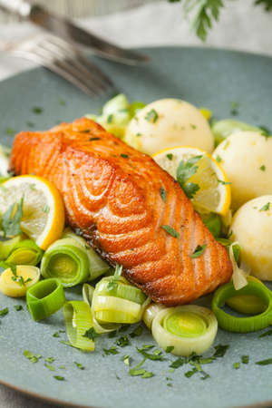 Portion of fried salmon, served with mashed potatoes and cooked leek. Front view. Gray plate, wooden background.の写真素材