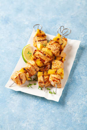 Grilled shashlik with salmon and pineapple. Served on paper try. Blue painted background.の写真素材