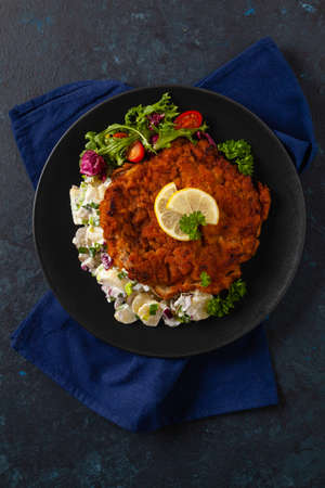 Classic, traditional Viennese sirloin schnitzel. Served on potato salad. Breaded. Dark background.の写真素材
