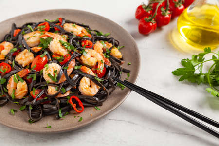 Black pasta with roasted prawns. Served on a plate. Stone background. Chopsticks or fork.の写真素材