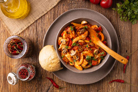 Chicken stew with peppers, mushrooms and tomatoes. Wooden background.の写真素材