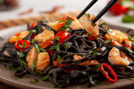Black pasta with roasted prawns. Served on a plate. Stone background. Chopsticks or fork.の写真素材