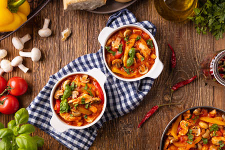 Chicken stew with peppers, mushrooms and tomatoes. Wooden background.の写真素材
