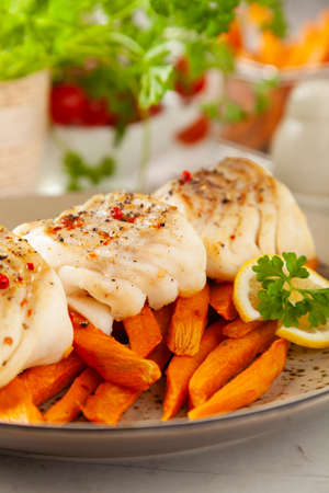 Fried pieces of cod loin, served with sweet potato fries. Light stone background.の写真素材