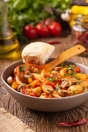Chicken stew with peppers, mushrooms and tomatoes. Wooden background.の写真素材
